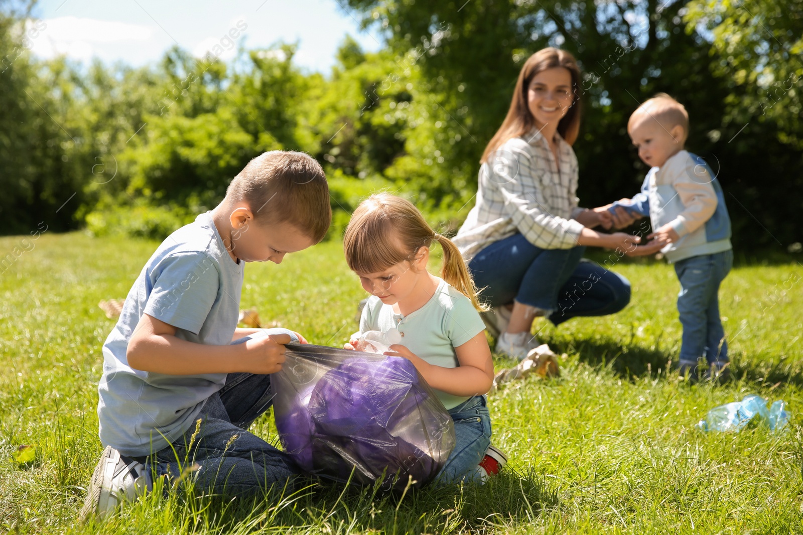 Photo of Mother and her children with plastic bags collecting garbage in park