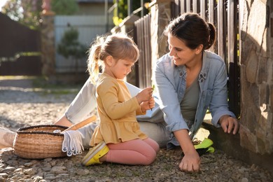 Photo of Mother and her cute daughter spending time together while pulling out grass near house on spring day