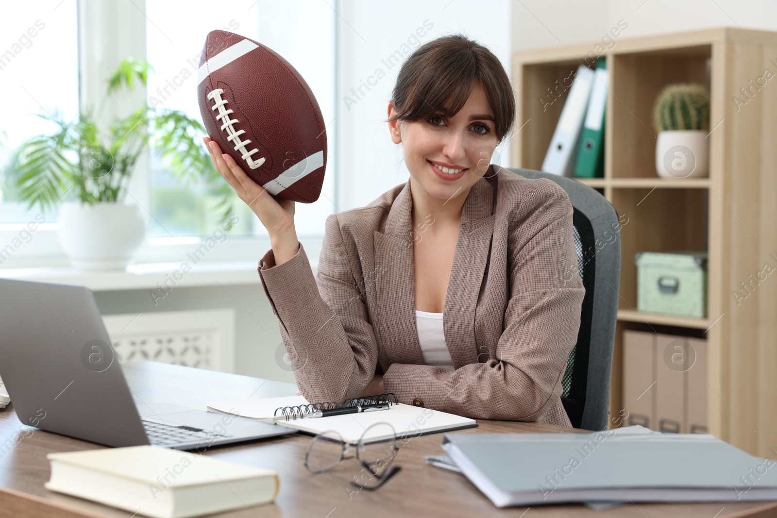 Photo of Smiling employee with american football ball at table in office