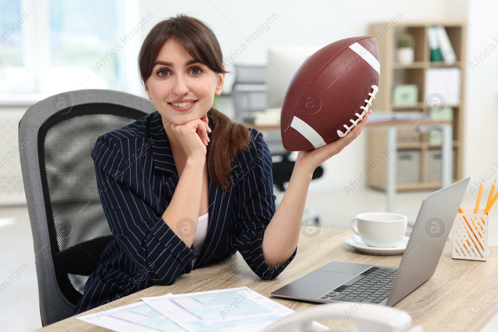 Photo of Smiling employee with american football ball at table in office