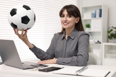 Smiling employee with soccer ball at table in office