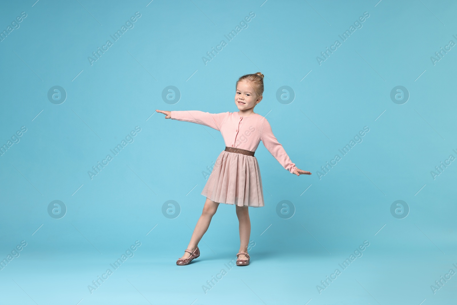 Photo of Cute little girl dancing on light blue background