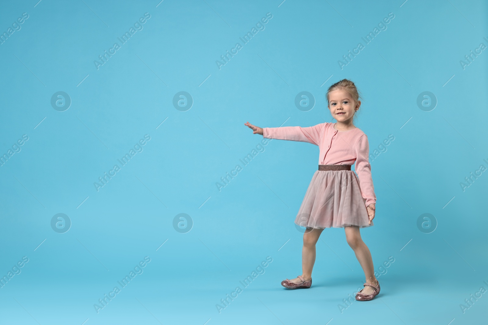 Photo of Cute little girl dancing on light blue background, space for text