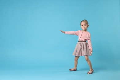 Cute little girl dancing on light blue background, space for text