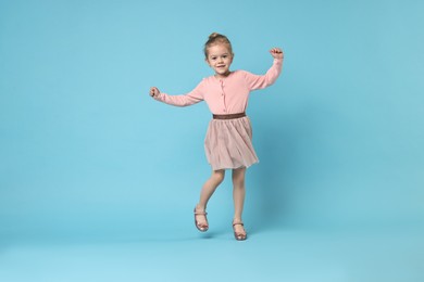 Cute little girl dancing on light blue background