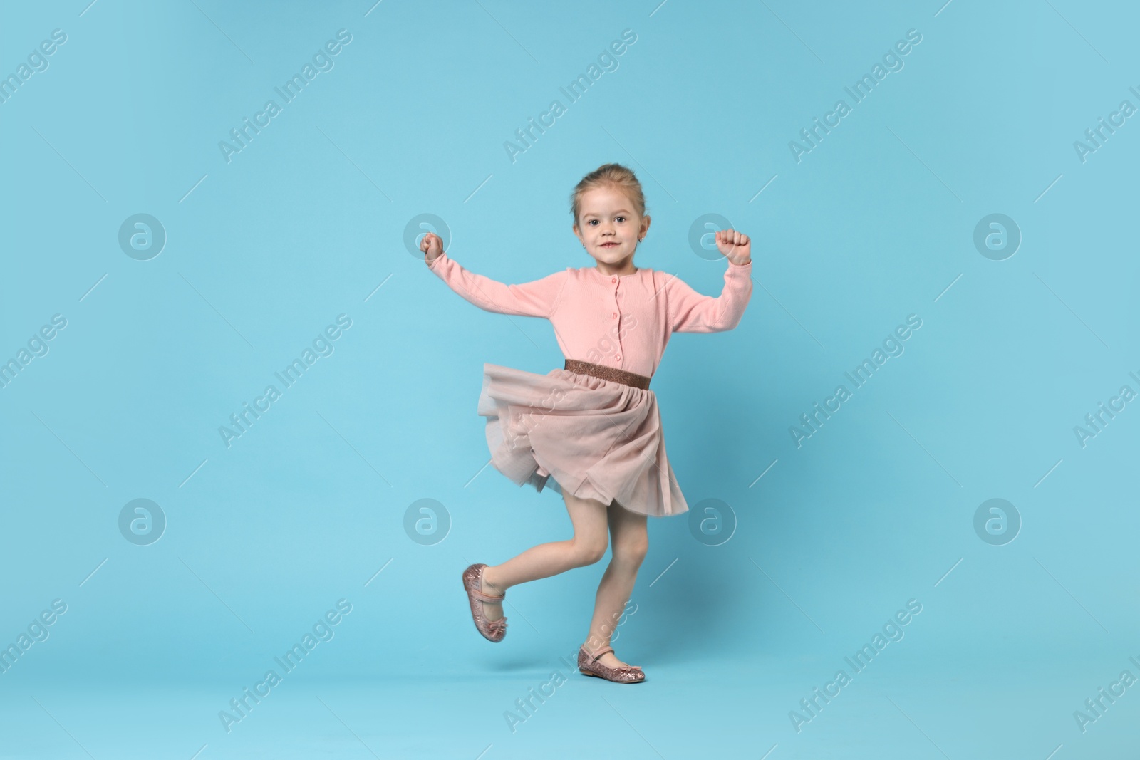 Photo of Cute little girl dancing on light blue background