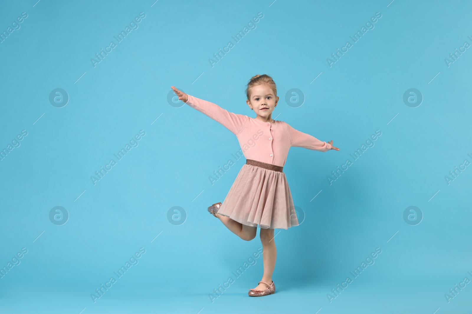 Photo of Cute little girl dancing on light blue background