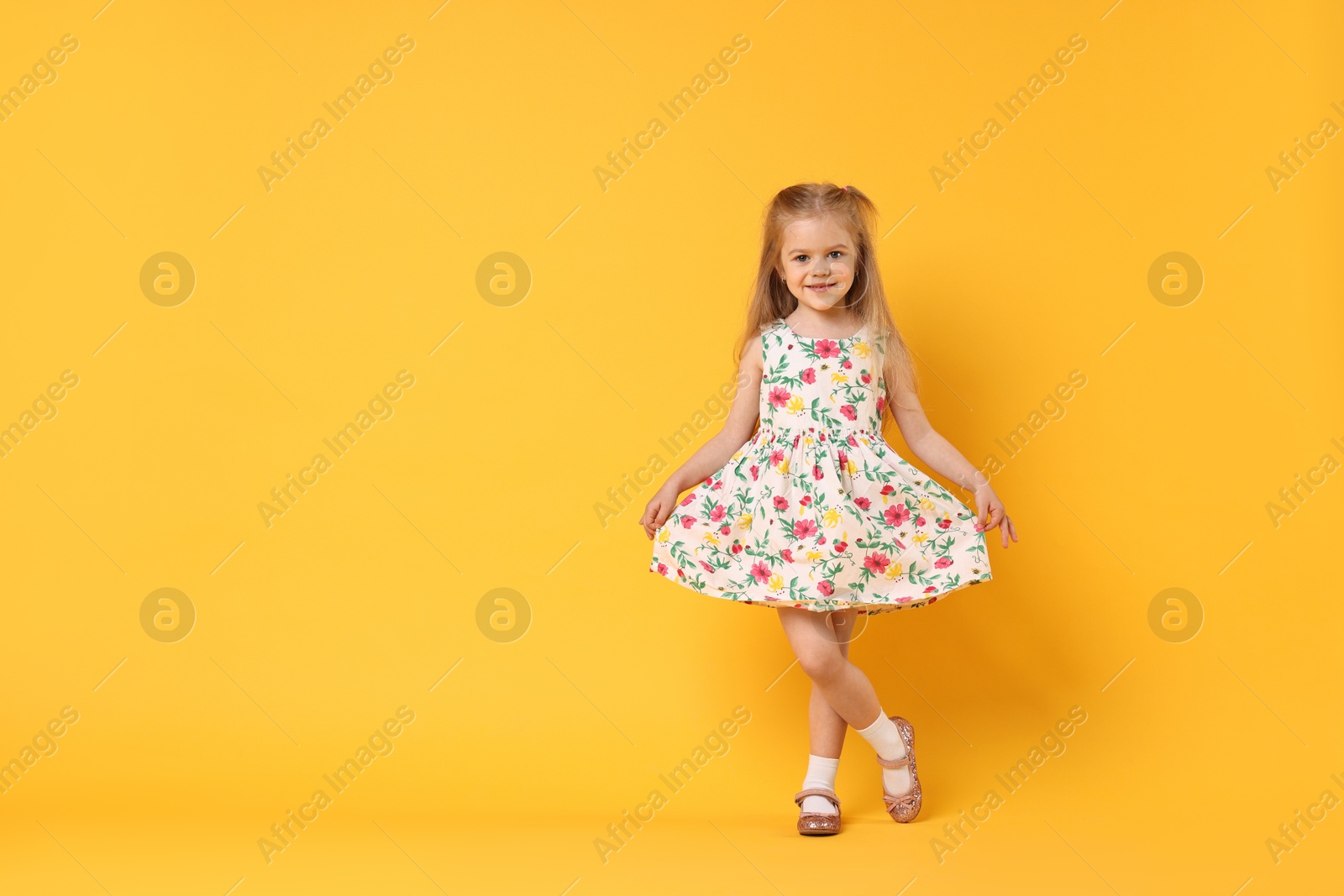 Photo of Cute little girl dancing on orange background, space for text