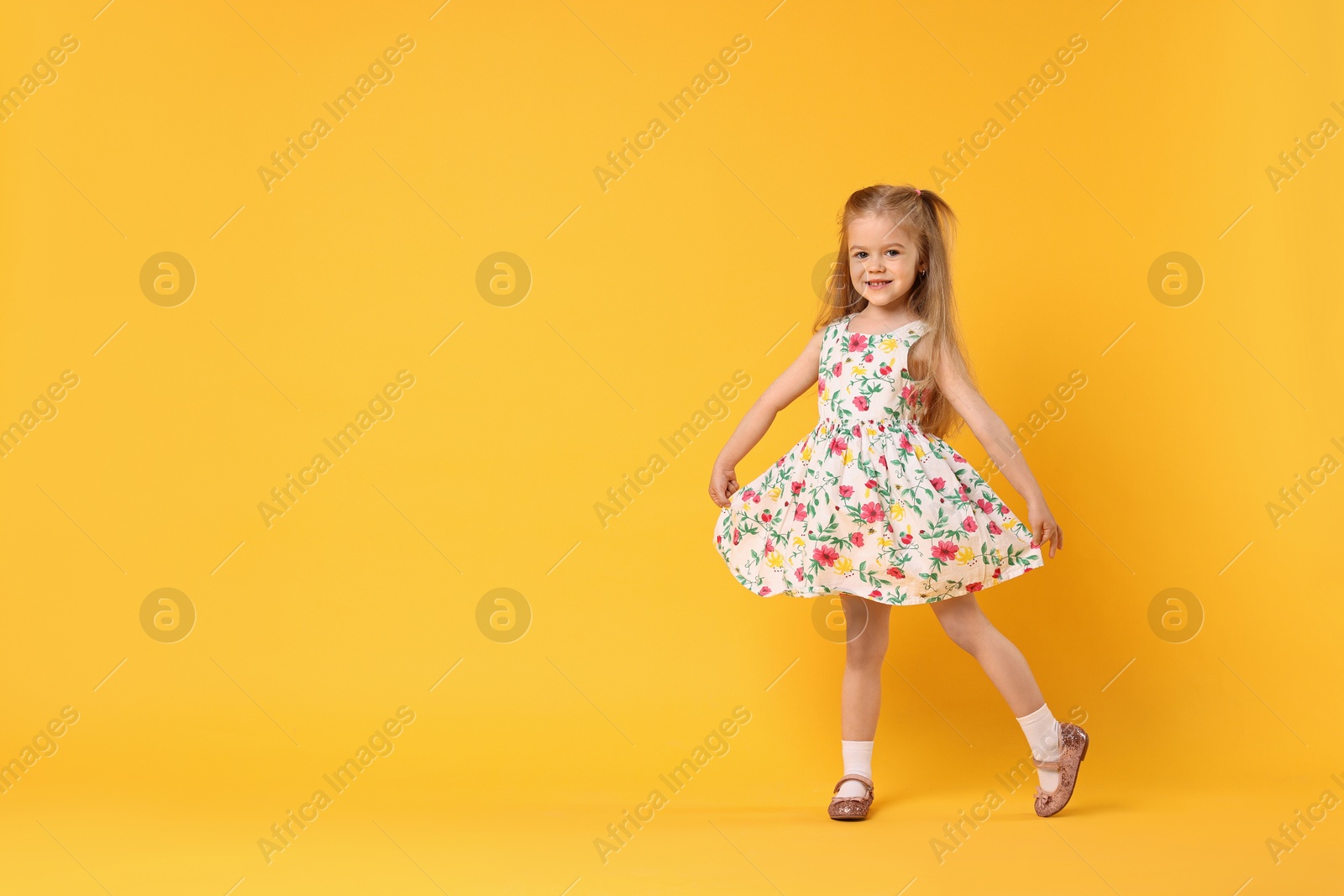 Photo of Cute little girl dancing on orange background, space for text