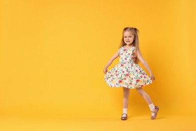 Photo of Cute little girl dancing on orange background, space for text