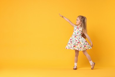 Photo of Cute little girl dancing on orange background, space for text