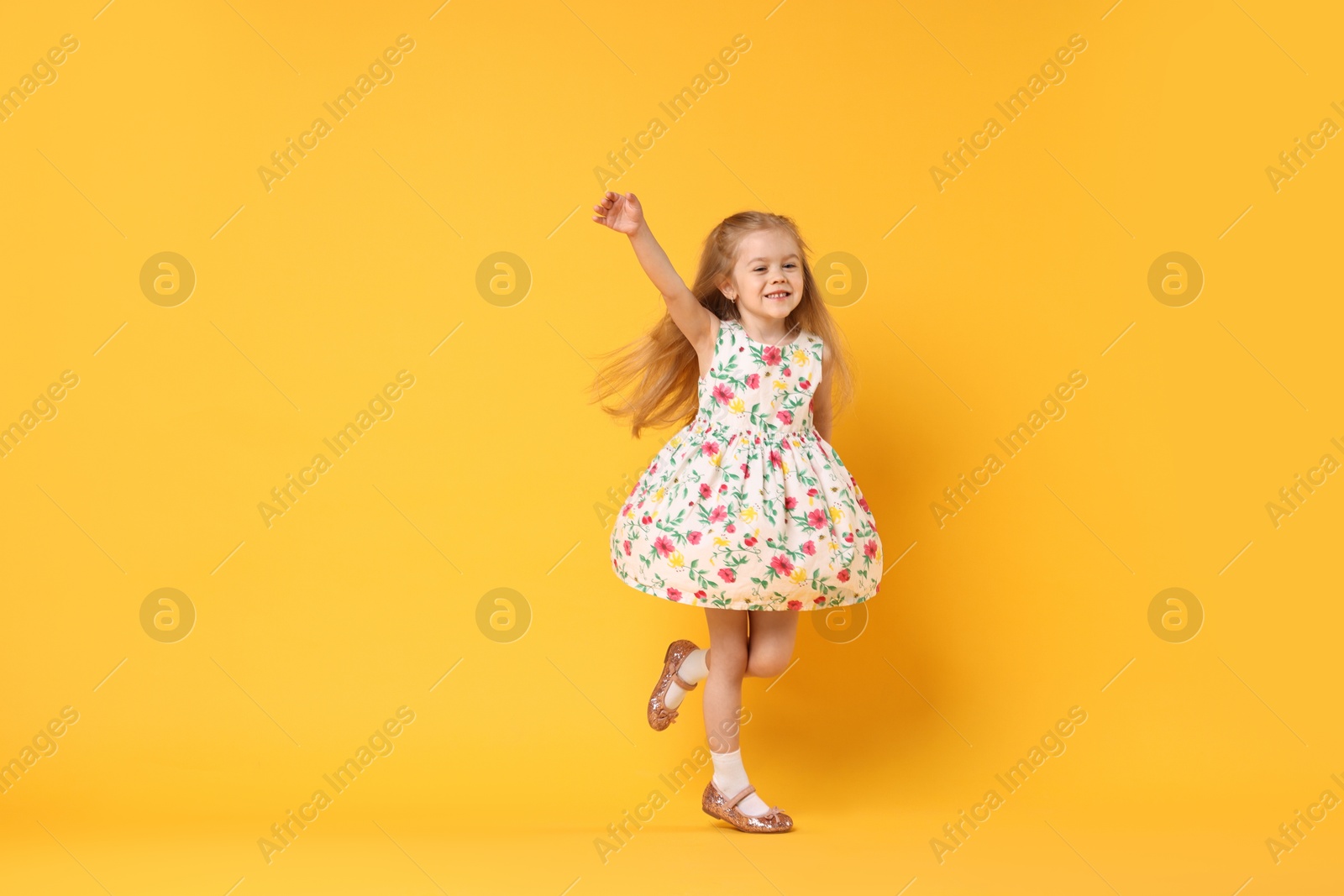 Photo of Cute little girl dancing on orange background