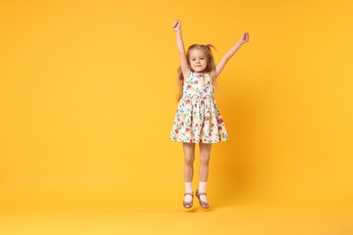 Photo of Cute little girl dancing on orange background, space for text