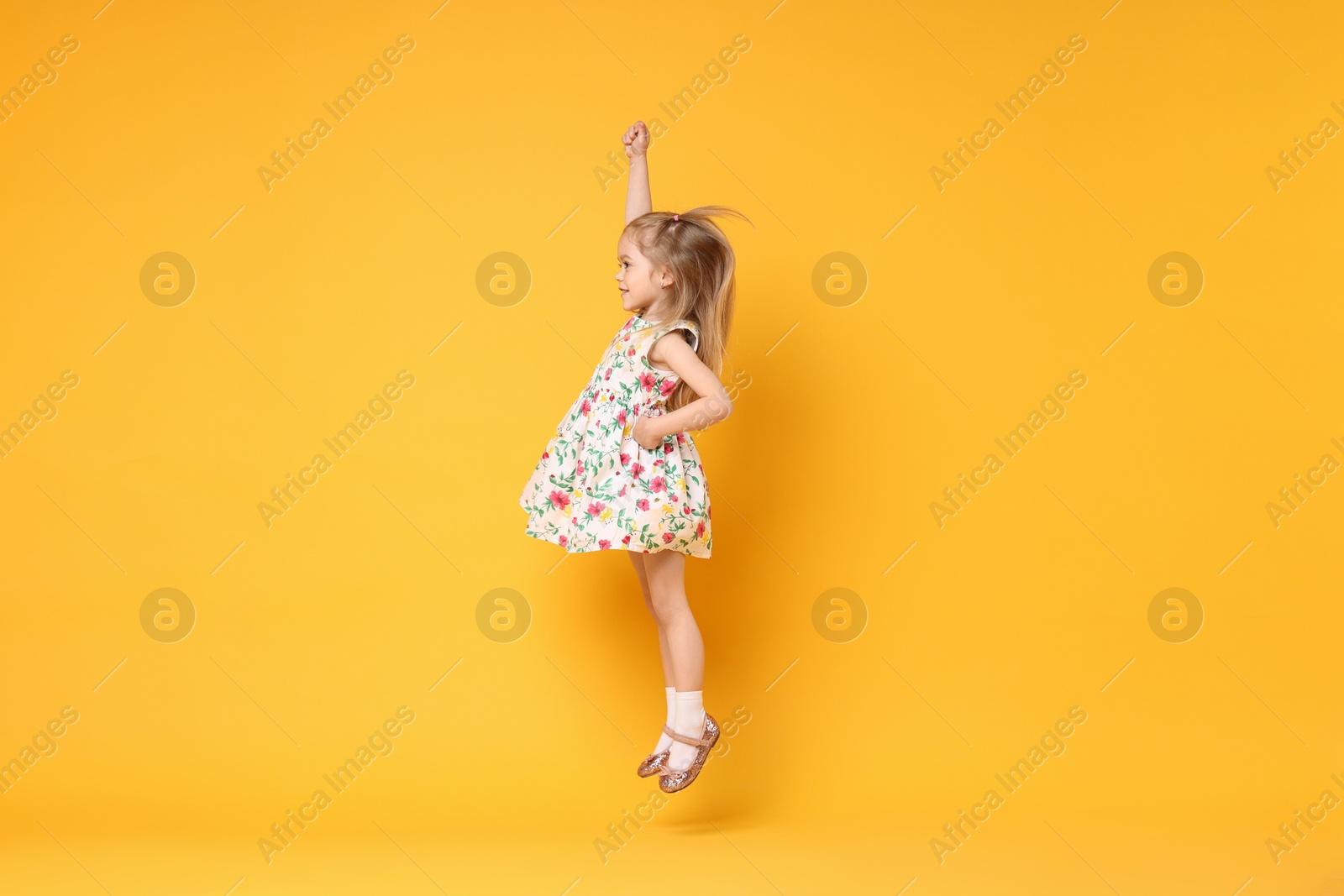 Photo of Cute little girl dancing on orange background