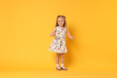 Photo of Cute little girl dancing on orange background