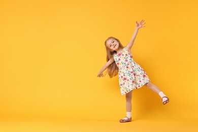 Photo of Cute little girl dancing on orange background, space for text