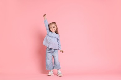 Photo of Cute little girl dancing on pink background, space for text