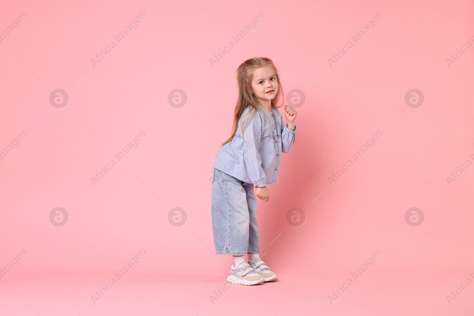 Photo of Cute little girl dancing on pink background