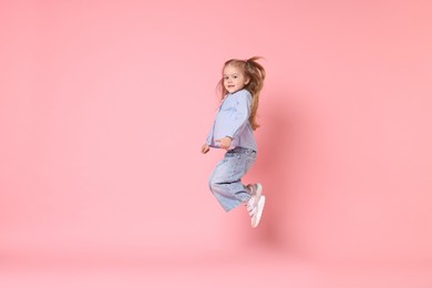 Photo of Cute little girl dancing on pink background, space for text