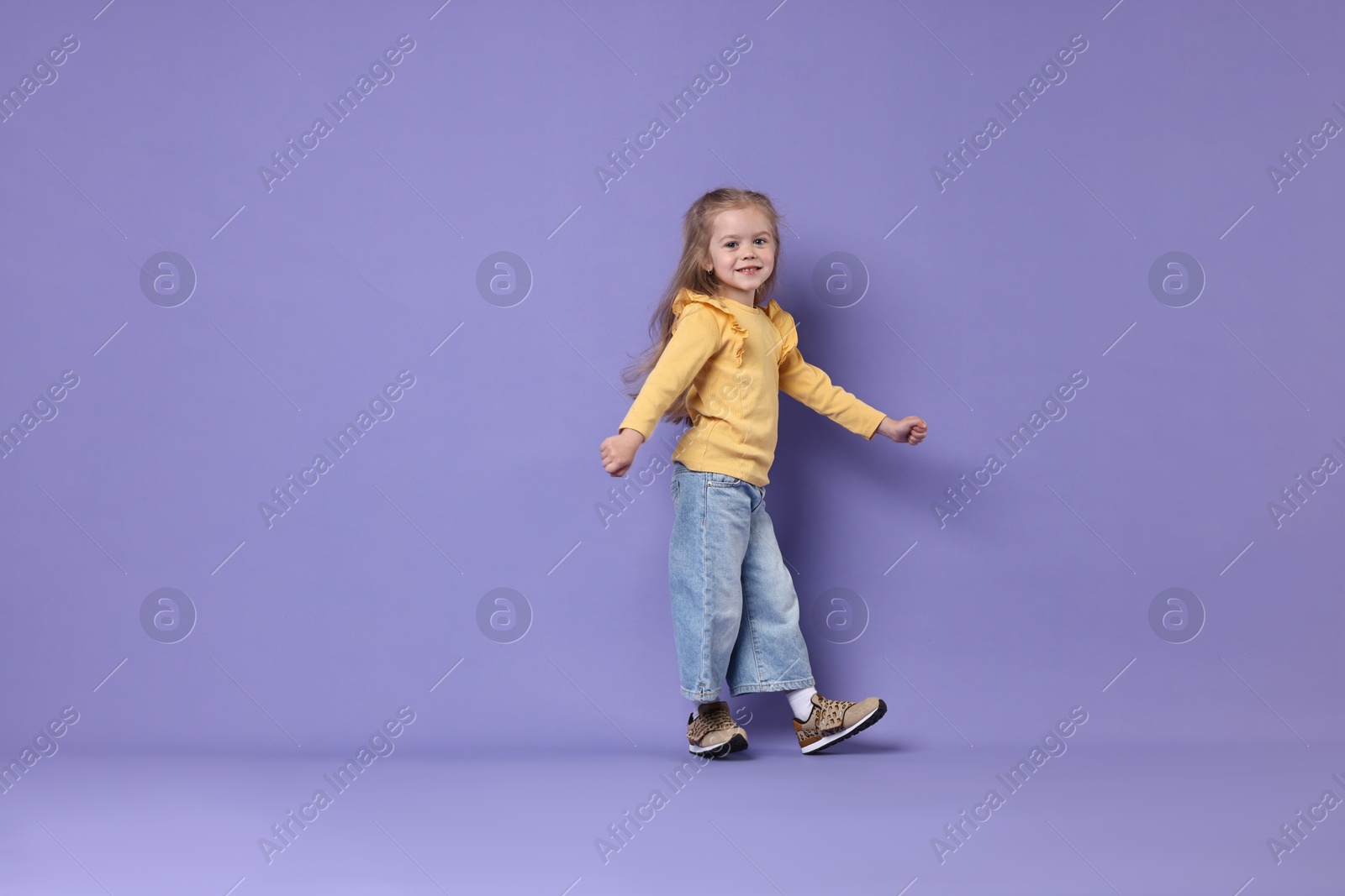 Photo of Cute little girl dancing on purple background