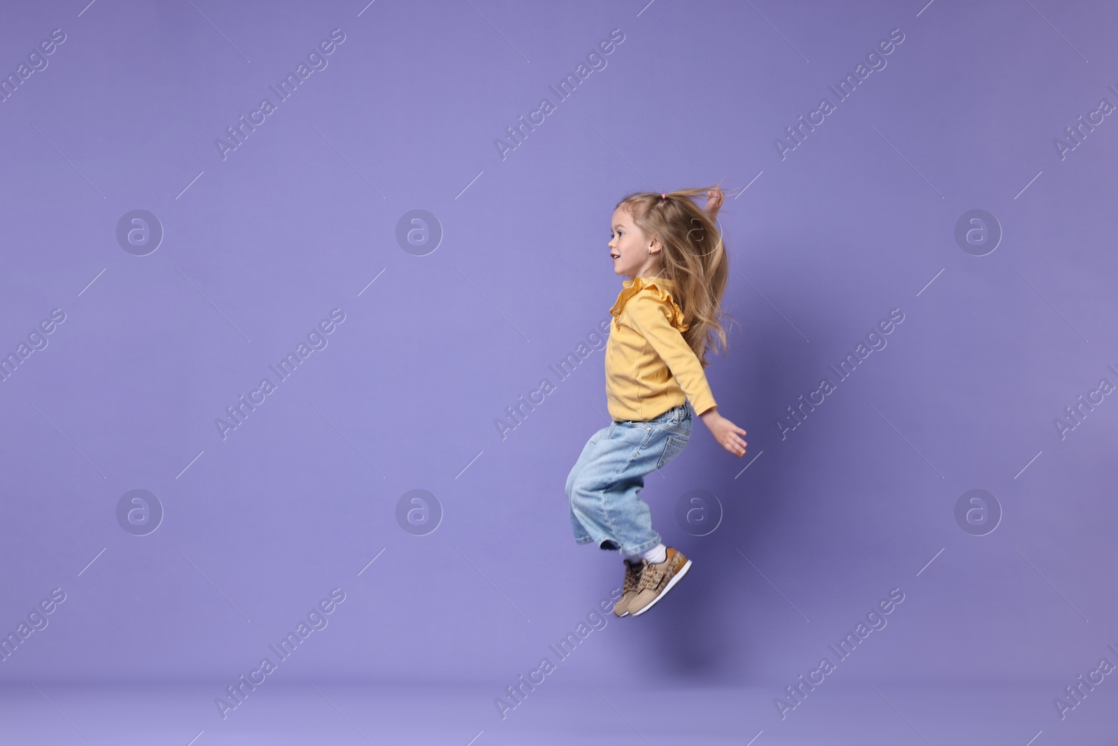 Photo of Cute little girl dancing on purple background, space for text