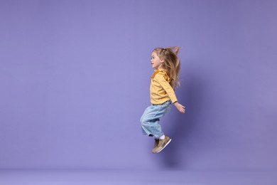 Photo of Cute little girl dancing on purple background, space for text