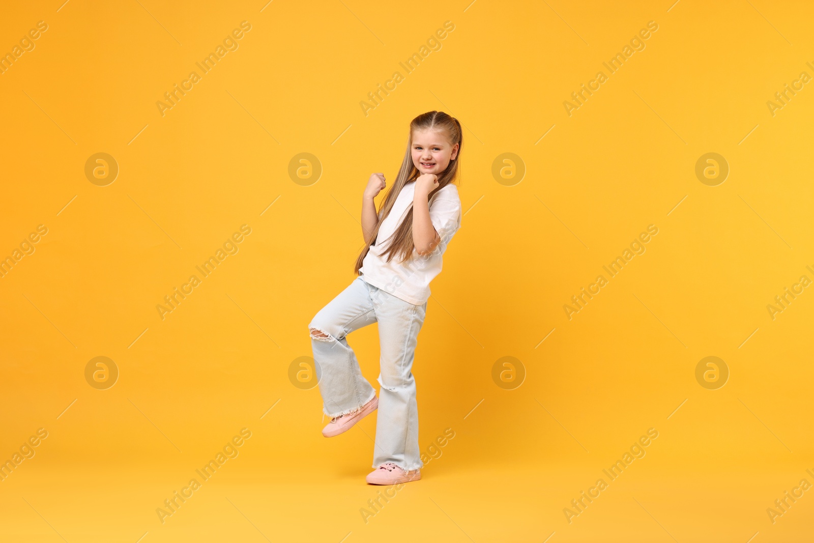 Photo of Cute little girl dancing on yellow background, space for text