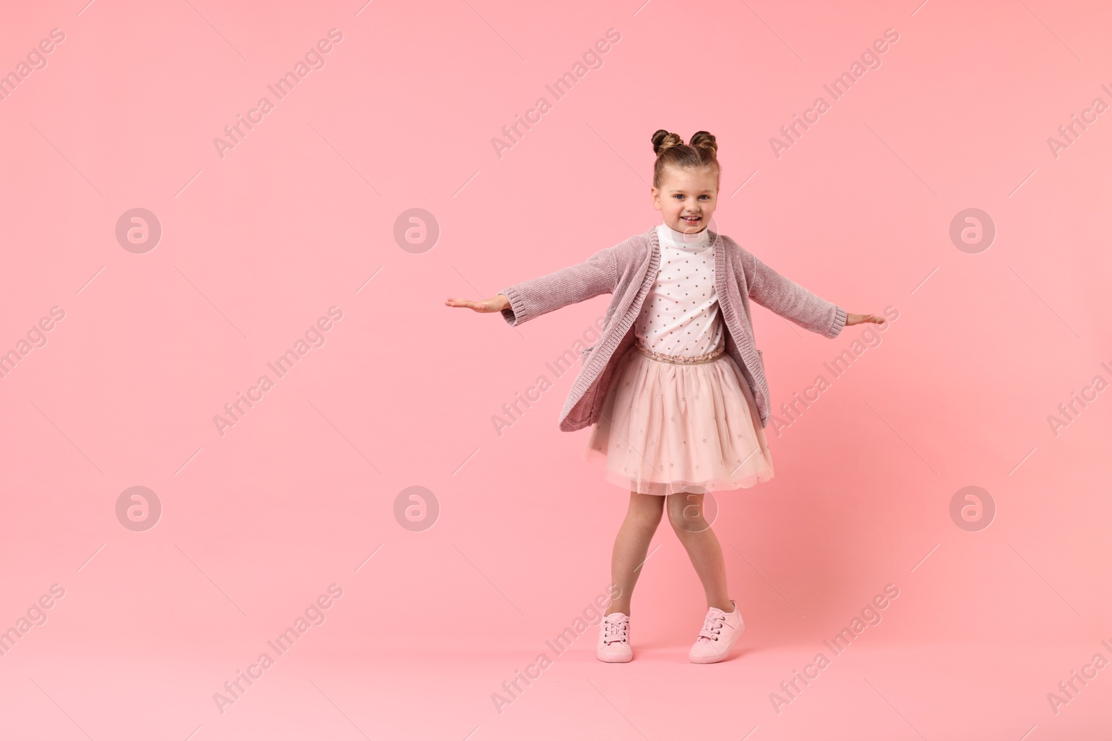 Photo of Cute little girl dancing on pink background, space for text