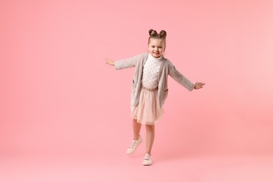 Photo of Cute little girl dancing on pink background, space for text