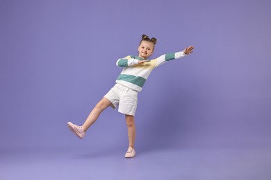 Photo of Cute little girl dancing on violet background