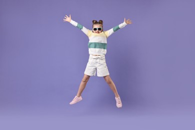 Photo of Cute little girl in sunglasses dancing on violet background