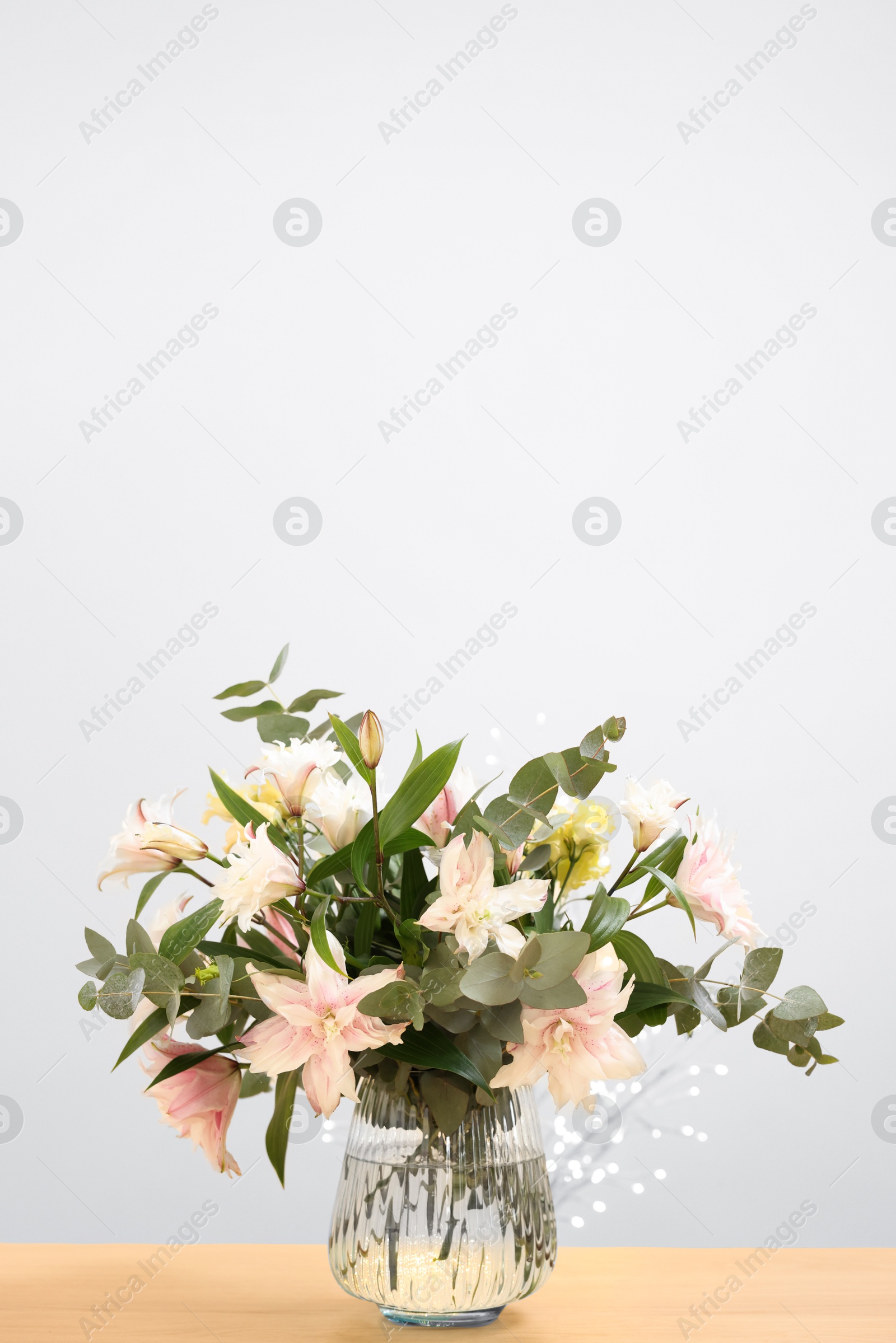 Photo of Bouquet of beautiful lily flowers in vase on wooden table against beige background, space for text