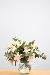 Photo of Bouquet of beautiful lily flowers in vase on wooden table against beige background, space for text