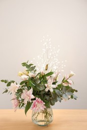 Photo of Bouquet of beautiful lily flowers in vase on wooden table against beige background