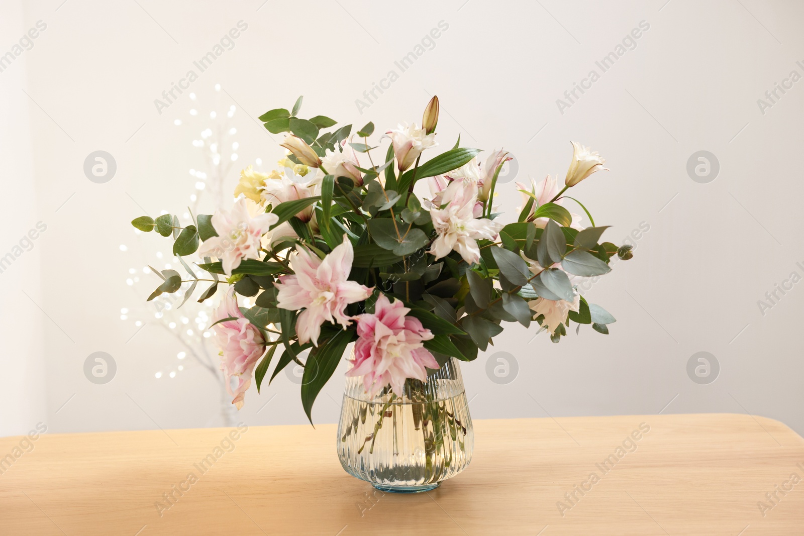 Photo of Bouquet of beautiful lily flowers in vase on wooden table against beige background