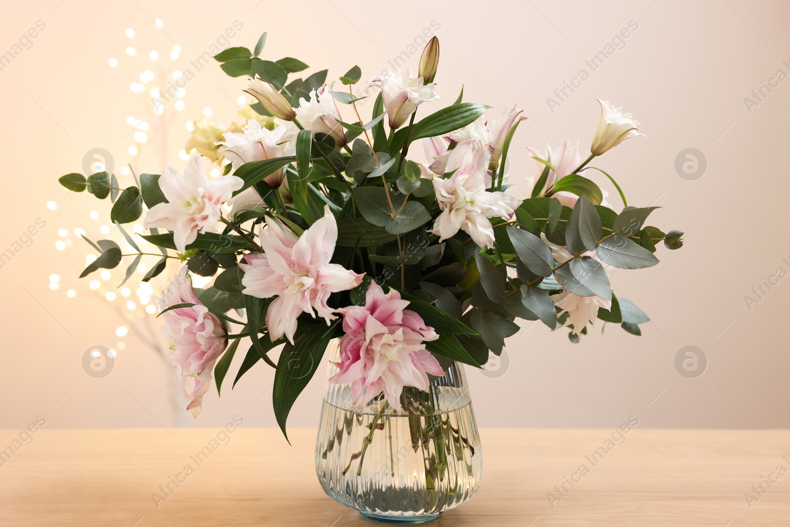 Photo of Bouquet of beautiful lily flowers in vase on wooden table against beige background