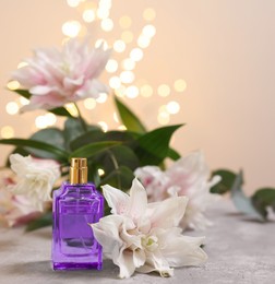 Photo of Bottle of perfume and beautiful lily flowers on table against beige background with blurred lights, closeup