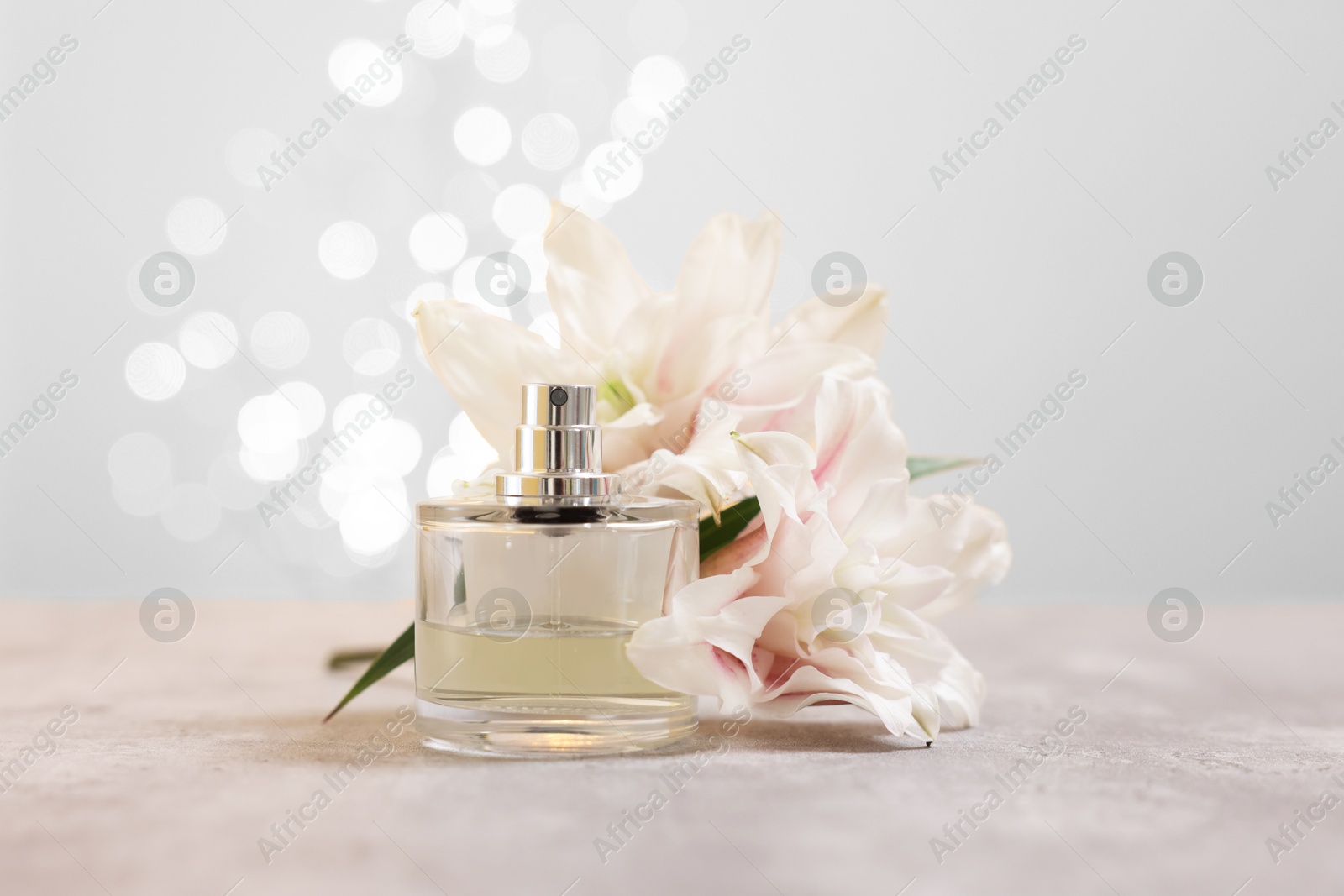 Photo of Bottle of perfume and beautiful lily flowers on table against beige background with blurred lights