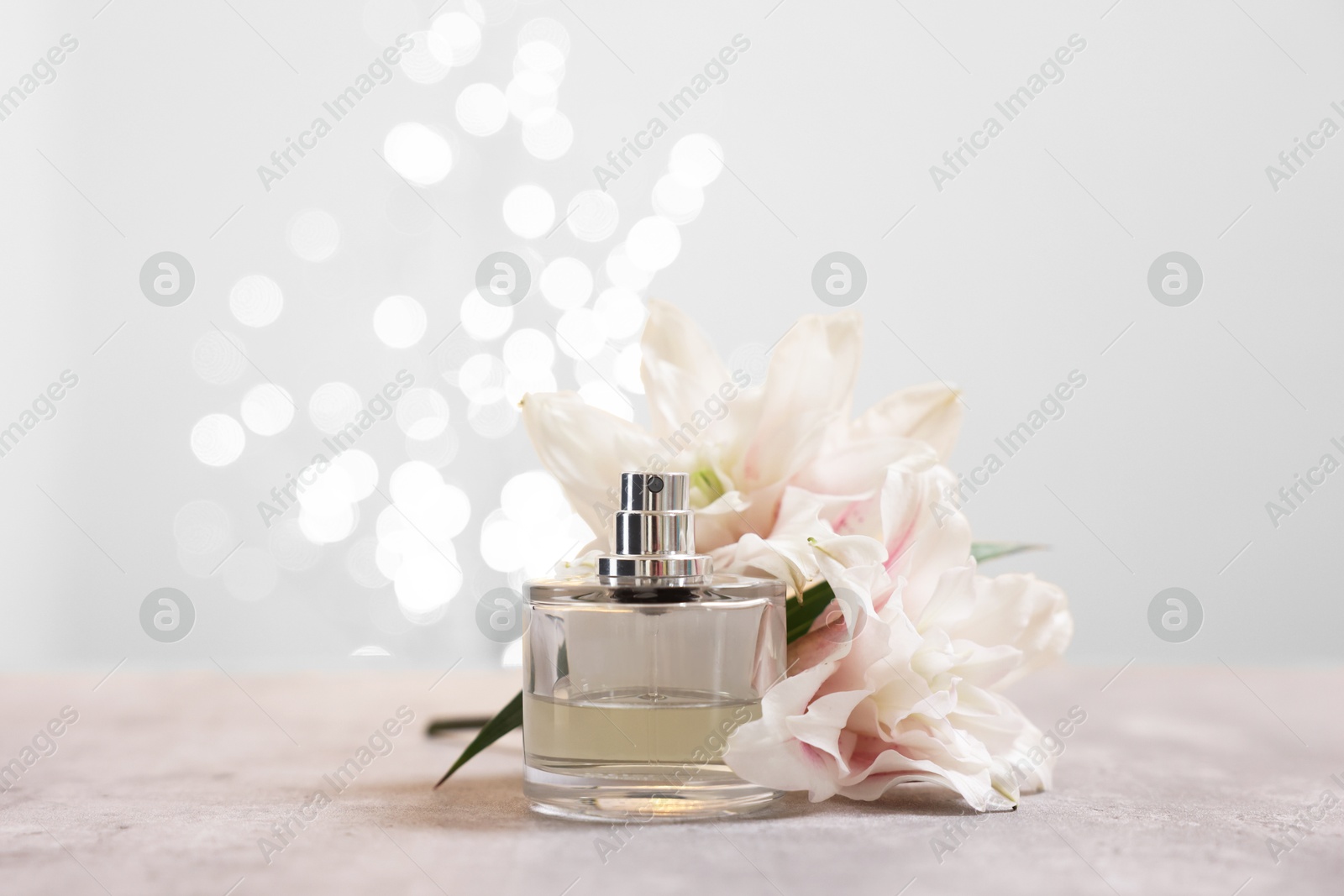 Photo of Bottle of perfume and beautiful lily flowers on table against beige background with blurred lights