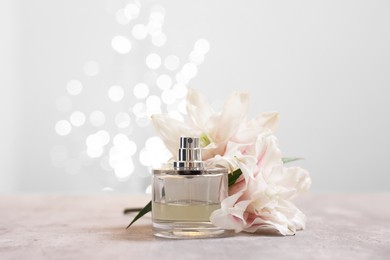 Photo of Bottle of perfume and beautiful lily flowers on table against beige background with blurred lights