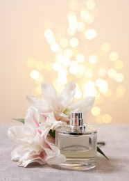 Bottle of perfume and beautiful lily flowers on table against beige background with blurred lights, space for text