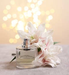 Photo of Bottle of perfume and beautiful lily flowers on table against beige background with blurred lights, space for text