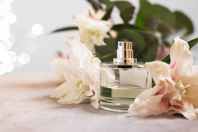 Photo of Bottle of perfume and beautiful lily flowers on table against beige background with blurred lights, closeup. Space for text