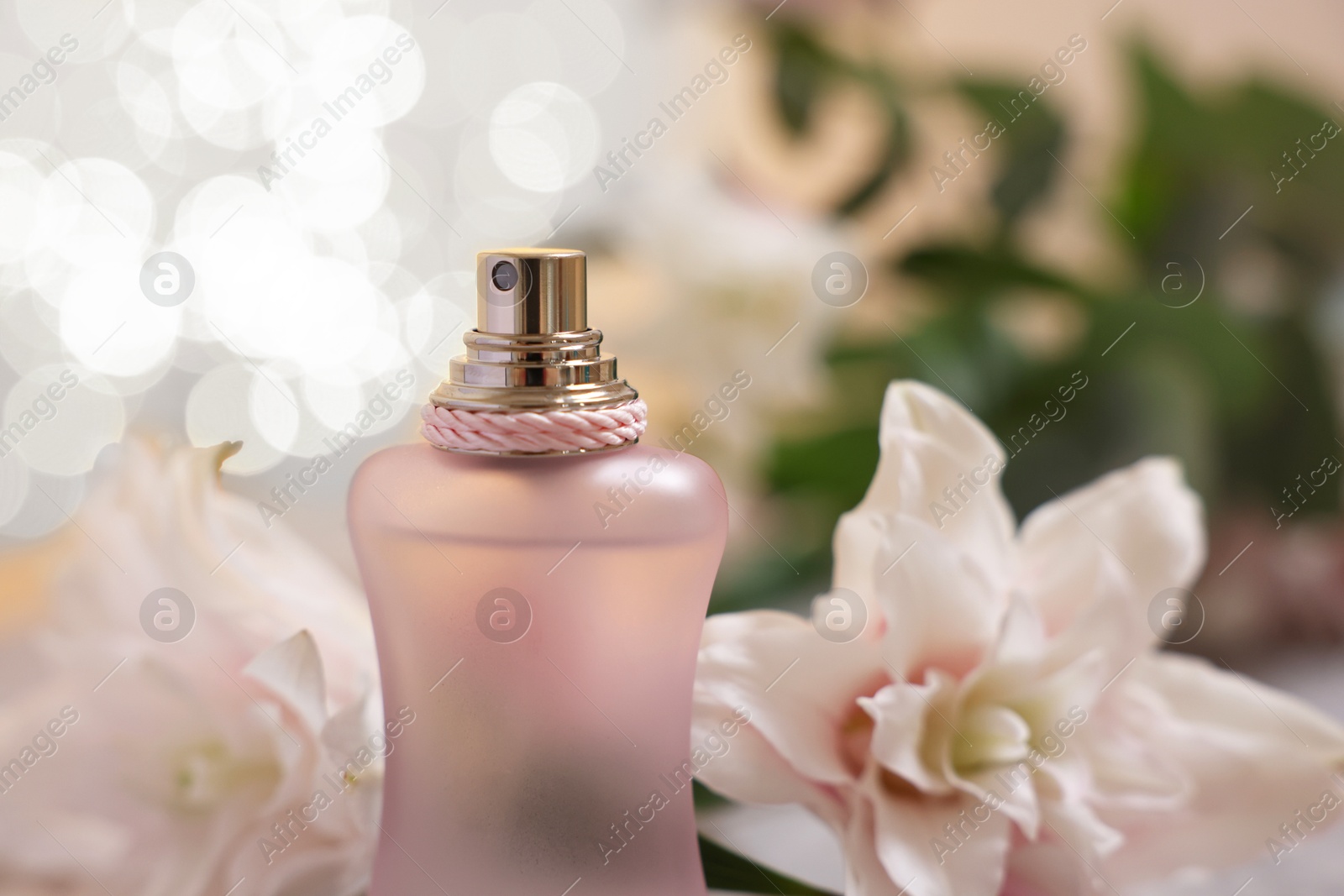 Photo of Bottle of perfume and beautiful lily flowers against beige background with blurred lights, closeup