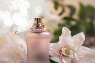 Photo of Bottle of perfume and beautiful lily flowers against beige background with blurred lights, closeup