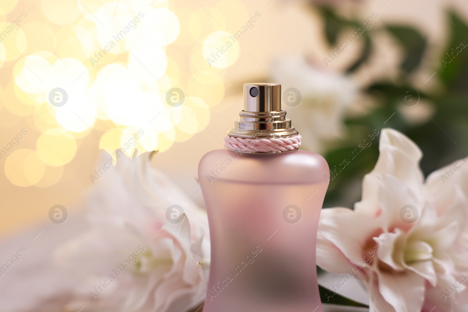 Photo of Bottle of perfume and beautiful lily flowers against beige background with blurred lights, closeup