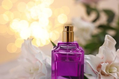 Photo of Bottle of perfume and beautiful lily flowers against beige background with blurred lights, closeup