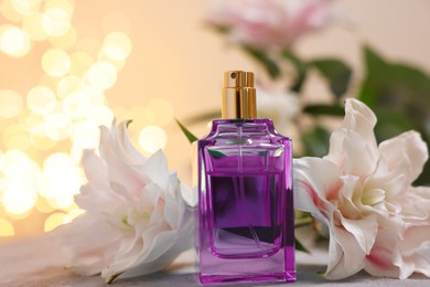 Photo of Bottle of perfume and beautiful lily flowers on table against beige background with blurred lights, closeup