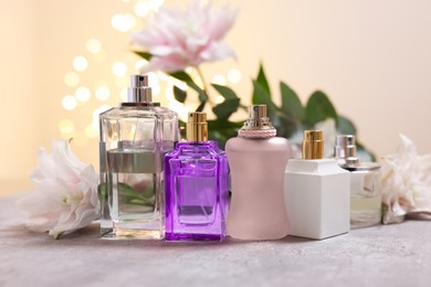 Photo of Perfume bottles and bouquet of beautiful lily flowers on table against beige background with blurred lights, closeup