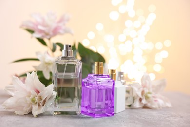 Perfume bottles and bouquet of beautiful lily flowers on table against beige background with blurred lights, closeup